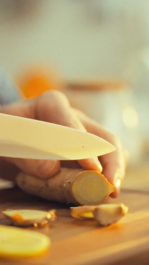 In a sunlit kitchen a chefs skilled hands chop fresh ginger root on a wooden Stock Footage 334398565