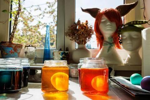 Sunlit kitchen craft scene with easter eggs soaking in a glass jars of yell.. Stock Photos