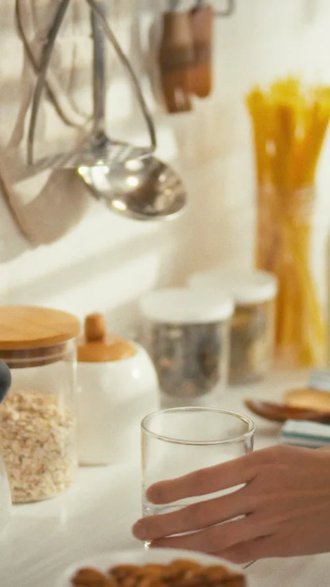 In sunlit kitchen filled with fresh ingredients person pours milk into a cle Stock Footage 331795200