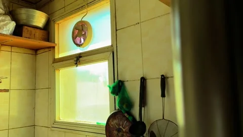 Sunlit Kitchen Window with Small Ventilation Fan and Rustic Shelves in Old Home Stock Footage 332073534