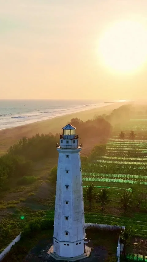 Sunlit lighthouse rising through golden coastal fields Stock Footage 335432460