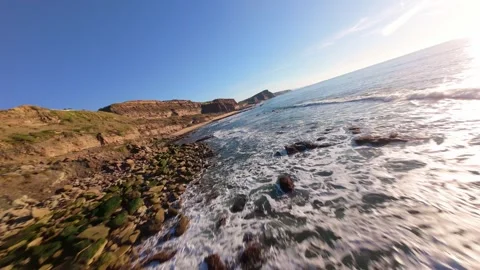 Sunlit ocean meets rugged cliffs with foamy waves Video stock 344560660