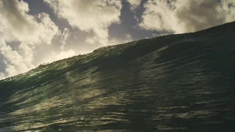 Sunlit Ocean Wave Crest Glowing Beneath Bright Clouds and Sky Stock Footage 344381175