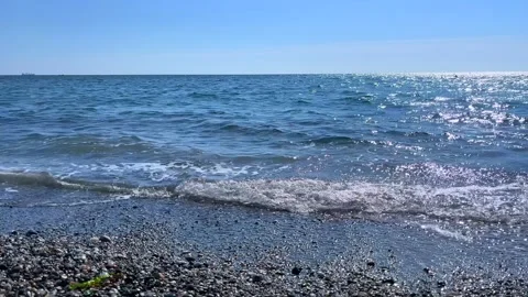 Sunlit Ocean Waves Crashing on Pebble Shore in Clear Blue Weather Stock Footage 310233485