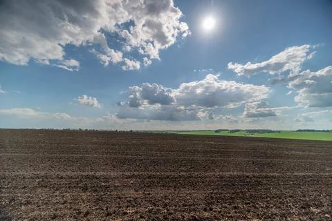 Sunlit plowed field under a dramatic cloud sky Stock Photos