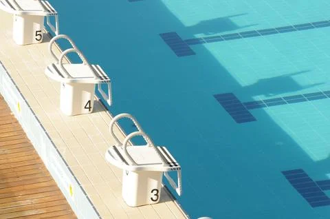 Sunlit pool with diving blocks casting shadows over crystal-clear water Stock Photos