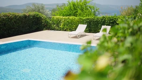 Sunlit private pool with blue mosaic tiles and two white loungers Stock Footage 327013629