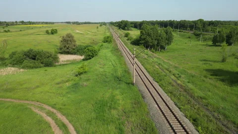 Sunlit railway track running through lush green meadow, revealing expansive Stock Footage 318315975