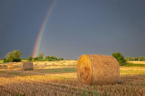 Sunlit rainbow over a post-harvest countryside field after rain. Stock Photos