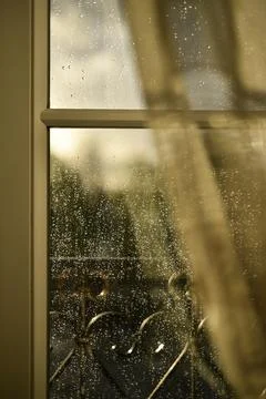 Sunlit raindrops on a windowpane with a soft glimpse of the window frame Stock Photos