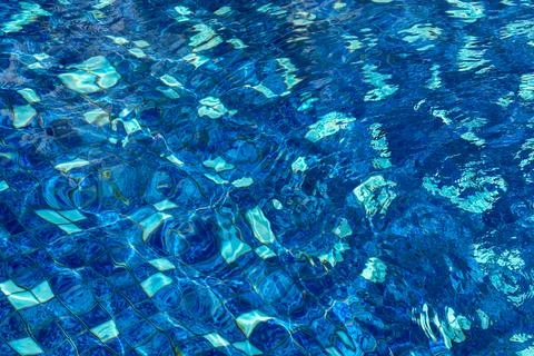 Sunlit ripples create vivid abstract patterns across clear blue swimming po.. Stock Photos