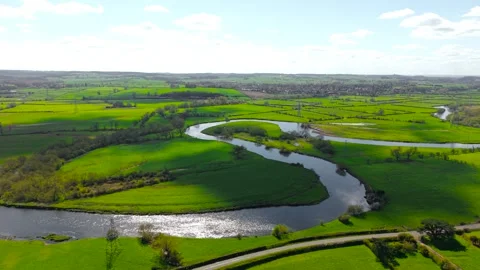 Sunlit river bend cutting across patchwork fields with strong light contrast 動画素材 339281129