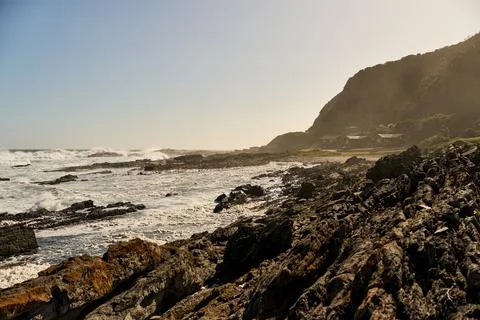 Sunlit Rocks Meet Rolling Waves. Peaceful Seaside View With Shadows And Rocky Stock Photos
