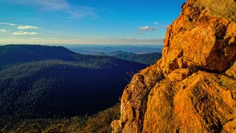 Sunlit rocky mountain peak overlooking vast forest valley landscape during Stock Footage 343696476