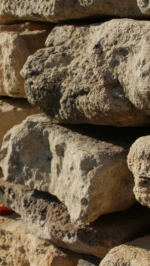 Sunlit rough stone wall with varied rocks and single red leaf Video stock 330237363