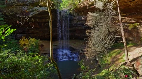Sunlit Sanctuary: A Cascading Waterfall in a Secluded Forest Grotto Video stock 323975786