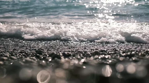 Sunlit sea waves gently breaking over a pebble shoreline. Sparkling water Stock Footage 325738721