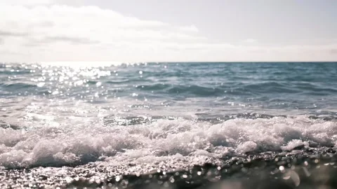 Sunlit sea waves gently breaking over a pebble shoreline. Sparkling water Stock Footage 325738773