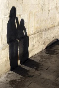Sunlit Shadows of Two People With Hot Drinks Walking Along a Wall. Stock Photos
