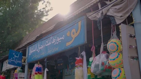 Sunlit shopfront in Tharparkar, Sindh with Urdu signboard and colorful hanging Stock Footage 328985700