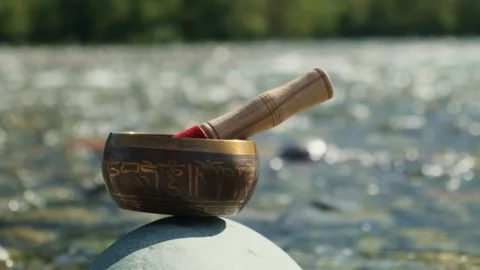 Sunlit singing bowl standing on the stone by the mountain stream. Stock Footage 291295344