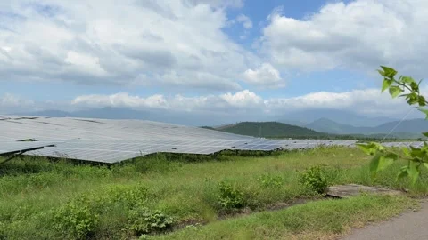 Sunlit solar panels follow sloping ground with mirrored surfaces catching bright Stock Footage 322515034