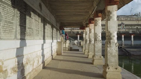 Sunlit Stone Pillar Corridor Beside Shivaganga Temple Tank with Devotees Stock Footage 338027117
