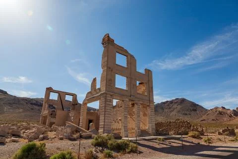 Sunlit stone ruins with empty window openings and desert mountains beyond a.. Fotos de archivo