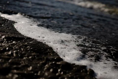 Sunlit Surf Breaking Over a Dark Shoreline with White Foam Stock Photos