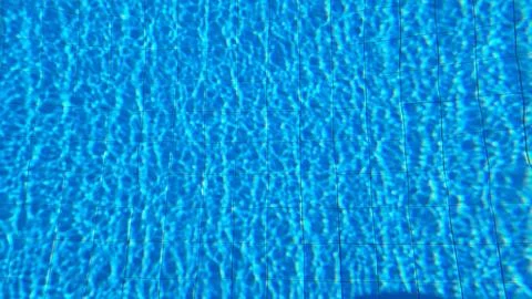 Sunlit Swimming Pool Water Surface with Blue Tiles and Ripple Reflection Pa.. Stock Photos