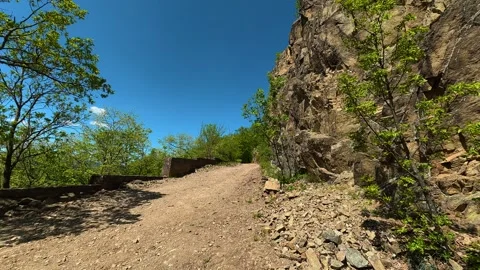 Sunlit trail winds past rocky cliffside. Balkan, Eastern Europe, POV Vídeo Stock 333350221