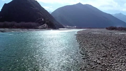 Sunlit turquoise river beside a pebble bank and layered mountains in Tibet Video stock 345884289