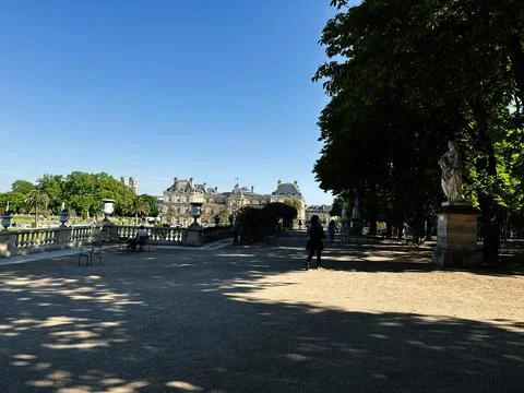 Sunlit walkway, classical statues and the Luxembourg Palace framed by trees.. Stock Photos