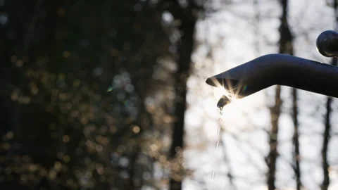 Sunlit Water Drops Falling from an Outdoor Faucet Stockbeeldmateriaal 338187170
