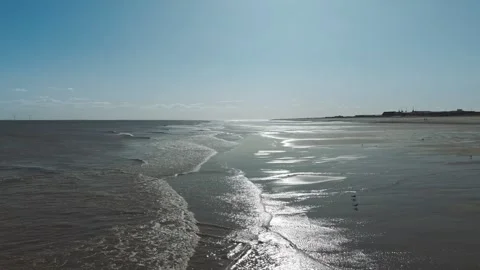 Sunlit waves gently lap the wet, reflective shore Stock Footage 346261114