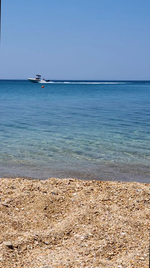 Sunny Beach With Clear Blue Water, Pebble Shore, And Speedboat On The Horizon Stock Footage 336300965