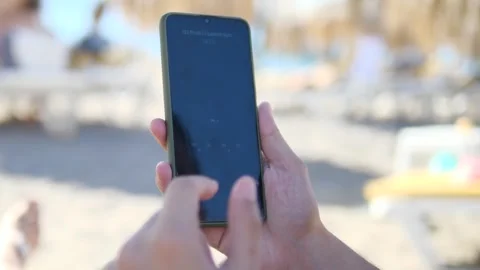 On a sunny beach, a mans hands hold a phone engaged in an audio-only video Stock Footage 318580933