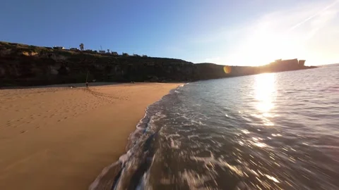 Sunny beach sunset, waves lap shore, cliffs rise high with green plants Stock Footage 344557491