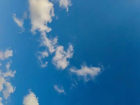 Sunny clear deep blue sky background with scattered small white cumulus clouds. Stock Photos