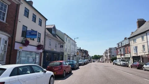 Sunny day driving through a quaint British high street with shops and cars Stock Footage 343614399