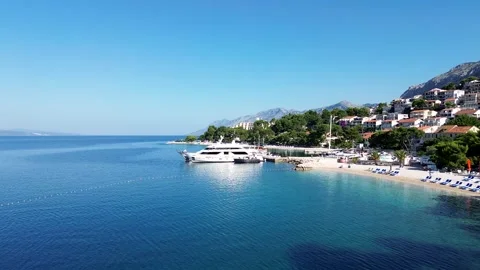 Sunny Drone Flyover of Brela Beach, Yacht, and Mountains – 4K Aerial Stock Footage 313900825