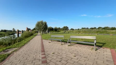 Sunny Riverside Walking Path with Bench in Green Park, 4K UHD Slow Camera Moveme Stock Footage 339716244