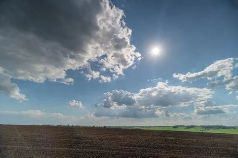 Sunny rural field under dramatic cloud sky Stock Photos