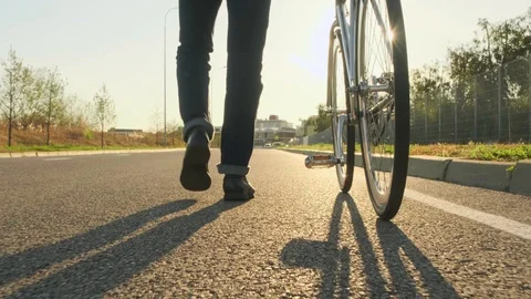 Sunny shot. Low angle, A man with a Bicycle is on the road, rear view. 스톡 동영상 121761427