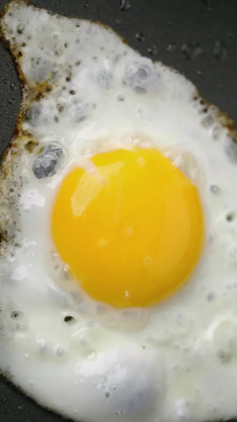 Sunny side up egg cooks in a pan with browned edges in closeup Stock Footage 344967750