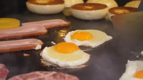 Sunny-Side Up Eggs, Ham, and Bacon Cooking on a Flat Top Flatstone Grill Vídeos de archivo 347687658