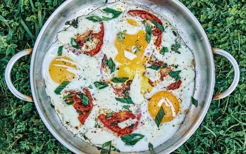 Sunny side eggs with tomatoes thyme onion and cheese in pan Stock Photos