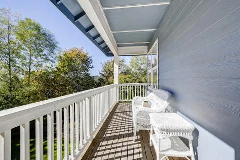 Sunny walkout deck with white wicker furniture. Blue house exterior. Northwes Stock Photos