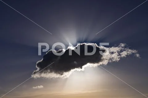 Sunrays bursting from behind a dark cumulus cloud Stock Photos