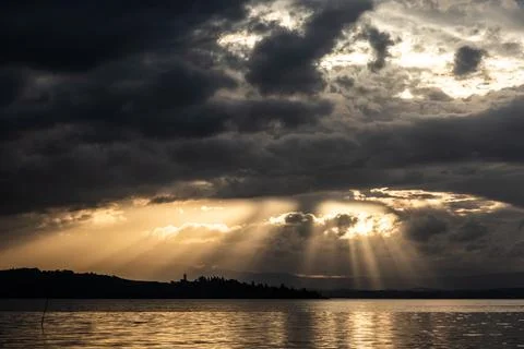 Sunrays at near sunset, with dark clouds in the background, above Trasimeno lake Stock Photos